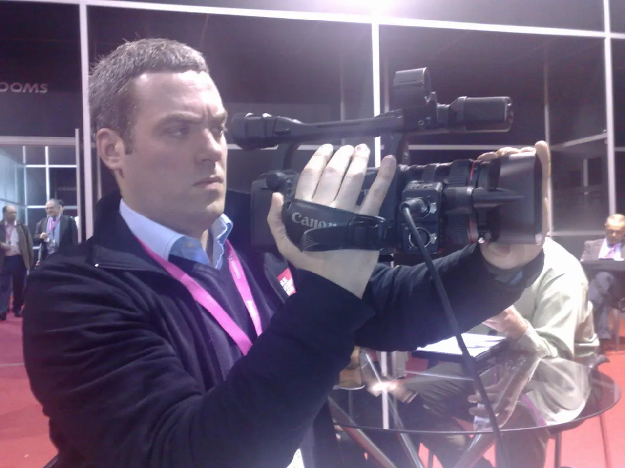 This picture describe that a man wearing black jacket and id card in this neck is holding the video...