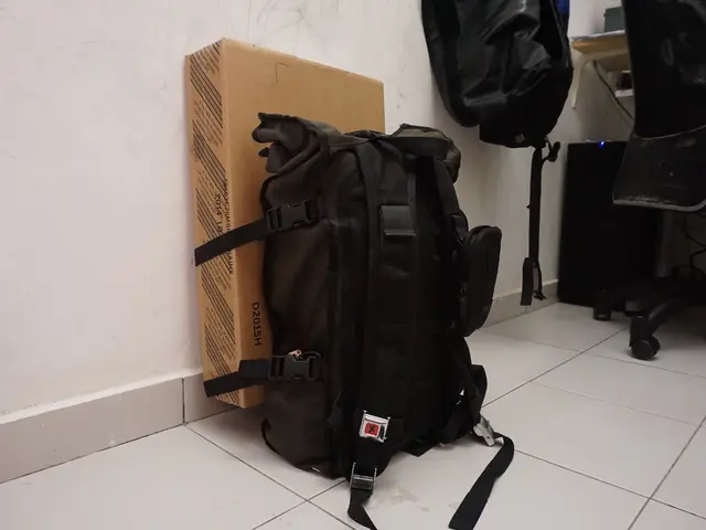 There is a backpack which is attached to a cardboard box and at the right side of the image there...